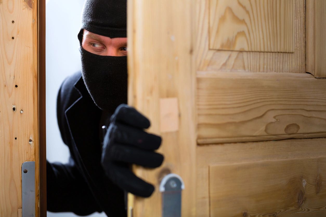 A person in black mask and gloves opening door.