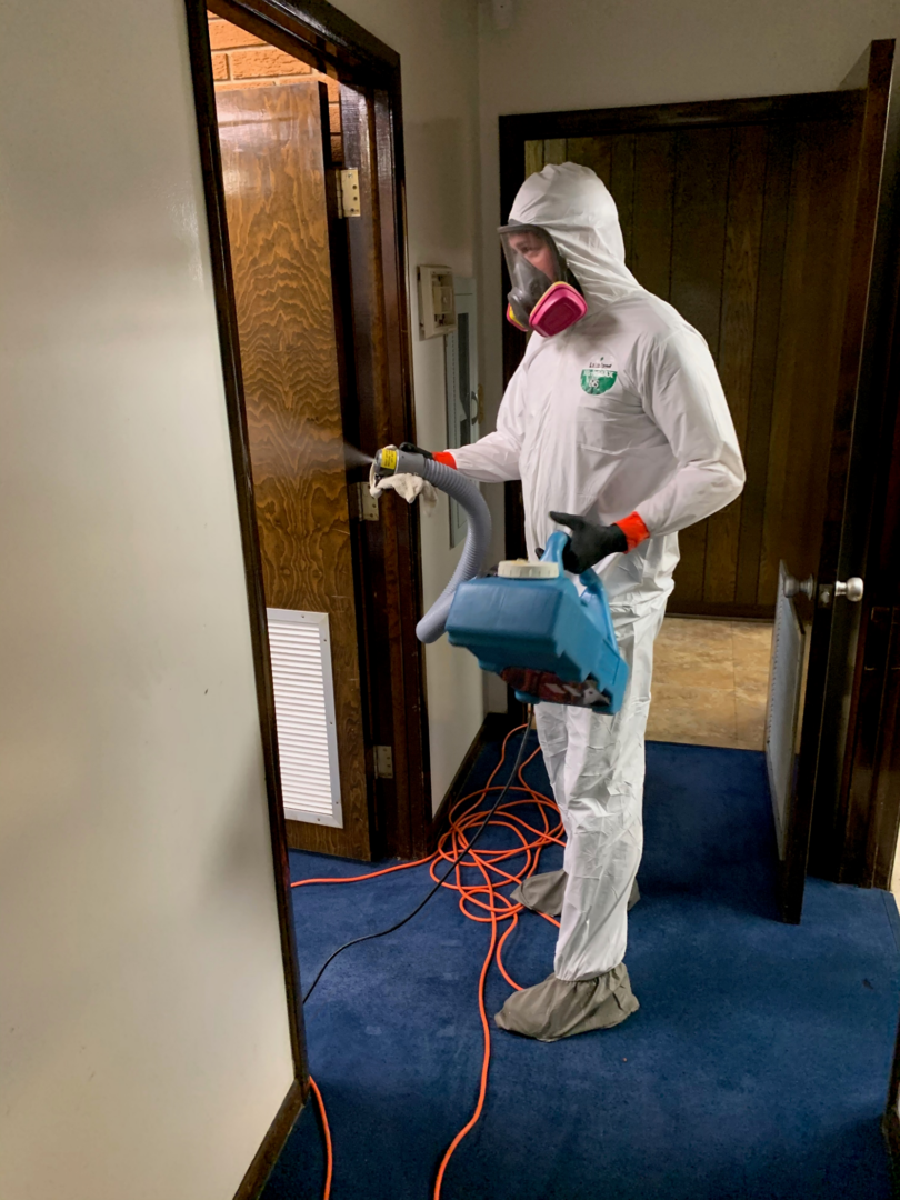 A person in white suit and mask holding a blue vacuum.
